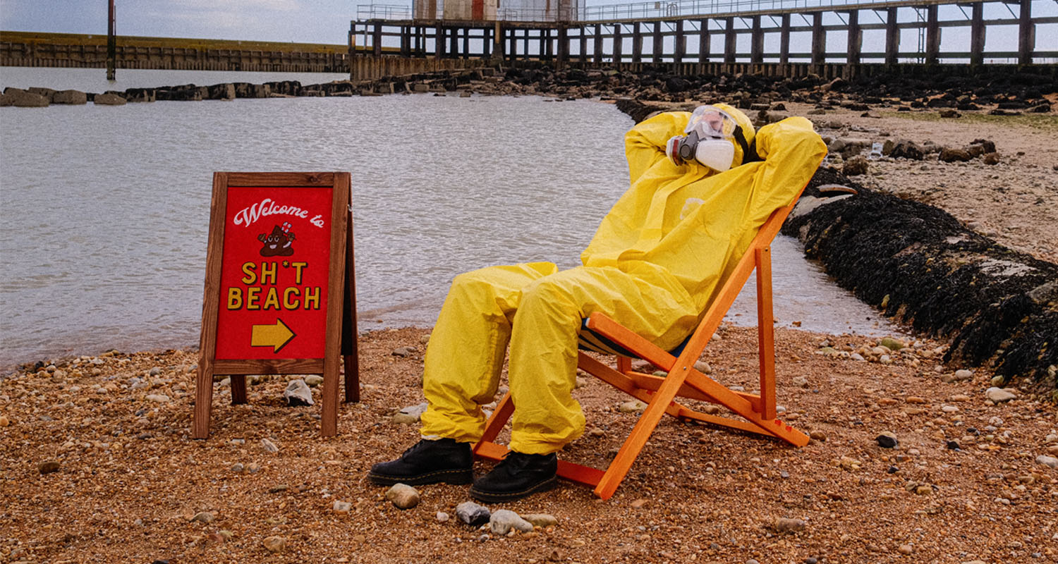 Person wearing a hazmat suit on a deck chair on a beach 