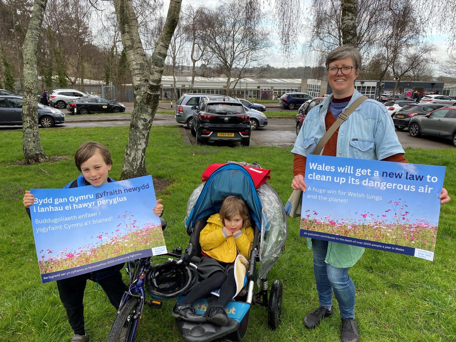 Image of woman and child holding posters demanding a strong clean air bill in Wales outside a school