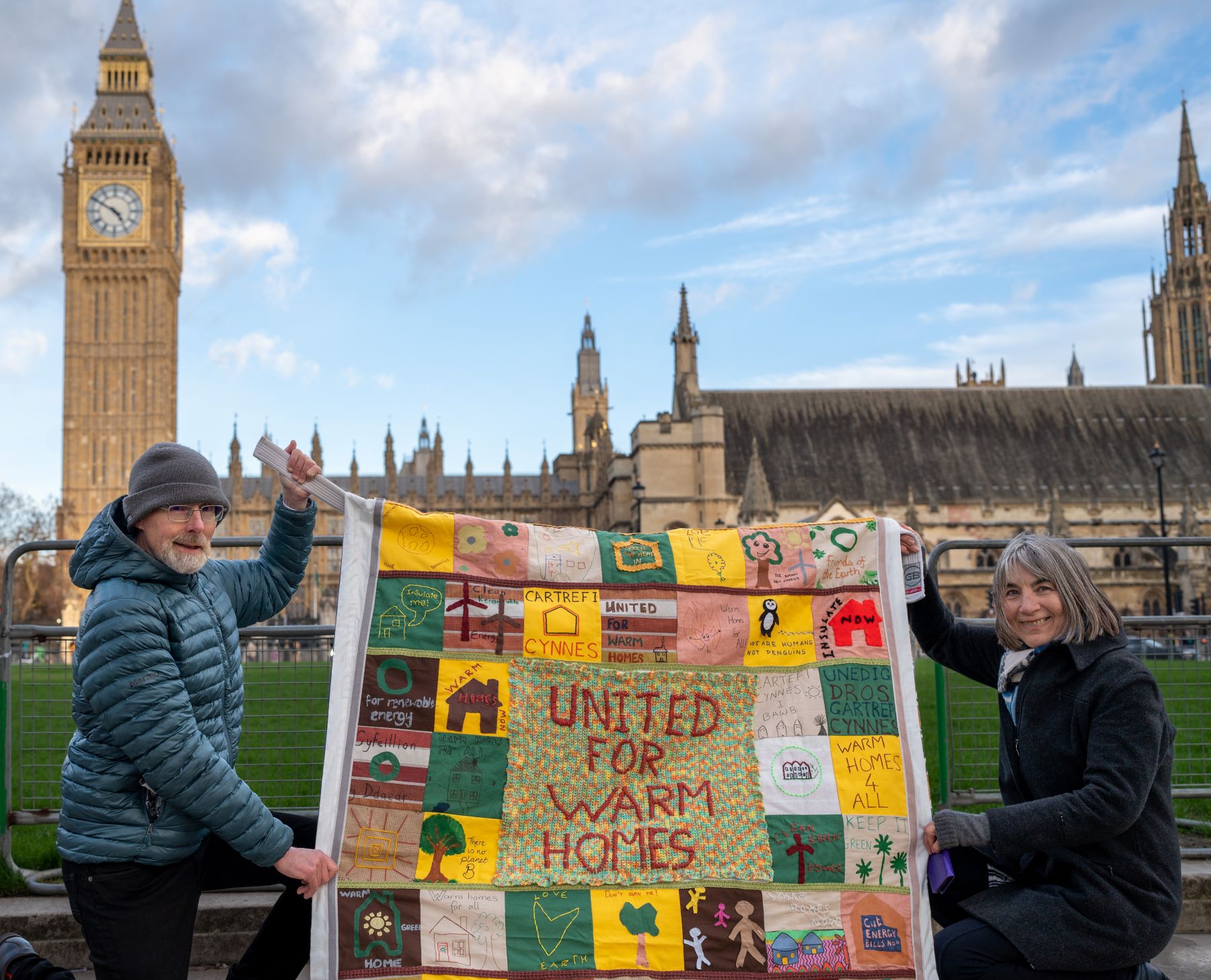 Two activists holding a united for warm homes hand quiltedbanner in front of Parliament 