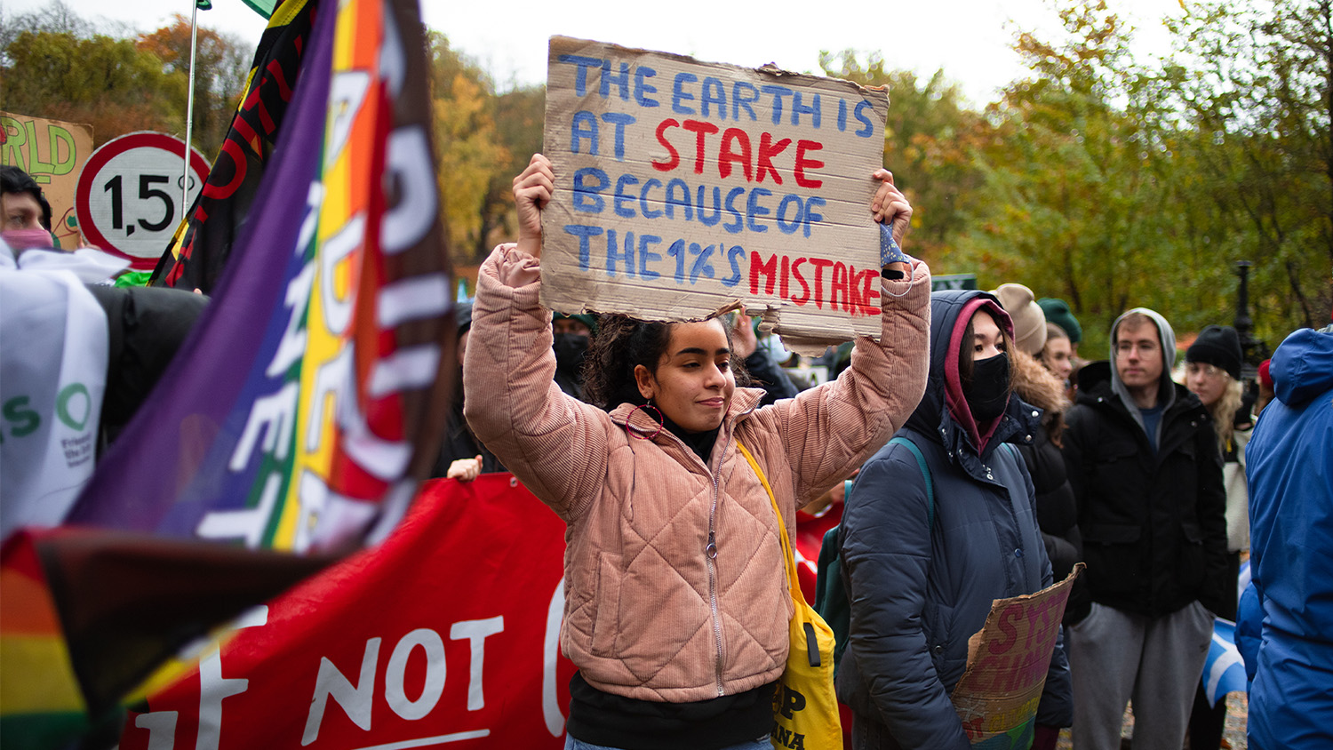 Image of a protest with a person holding up a placard that reads: the earth is at stake because of the 1%'s mistake 