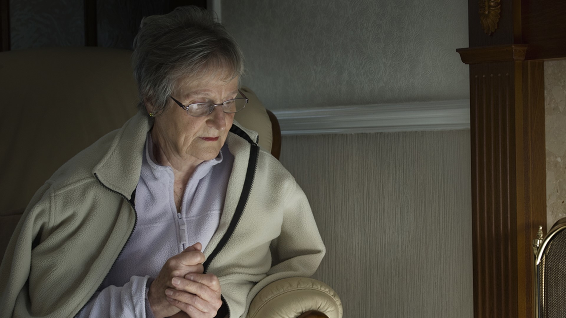Older woman in fleece next to radiator looking cold 